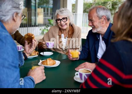 Mature grey haired woman smiling enjoying coffee with group friends on terrace of old people home. Stock Photo