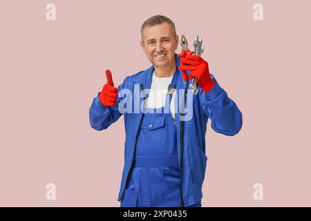Portrait of male mechanic with tools showing thumb-up on pink background Stock Photo