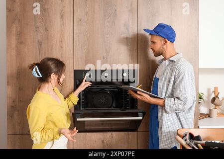 Young woman with male technician checking broken oven in kitchen Stock Photo