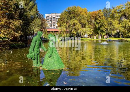 Razlog, Bulgaria, October 20, 2020: Lake, man and woman green leafs figurines panoramic view with autumn trees and fountains Stock Photo