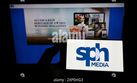 Stuttgart, Germany, 02-11-2022: Person holding smartphone with logo of Singaporean company SPH Media Limited on screen in front of website. Focus on Stock Photo