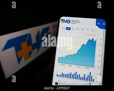 Stuttgart, Germany, 01-29-2022: Person holding cellphone with webpage of Thai company Thonburi Healthcare Group (THG) on screen in front of logo. Stock Photo