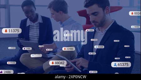 Image of social media notifications over diverse colleagues using tablet and laptop at work Stock Photo