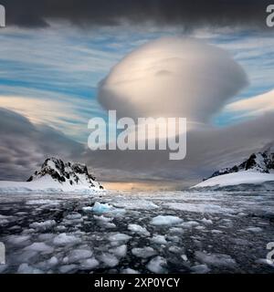 Lenticular cloud formation over the Lemaire Channel on the Antarctic Peninsula in Antarctica. Lenticular clouds are stationary saucer-shaped clouds that form in the troposphere, normally in perpendicular alignment to the wind direction. Stock Photo