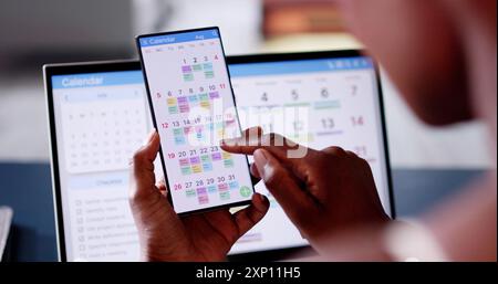 African Woman Organizing Appointment Schedule Using Cellphone And Calendar Stock Photo