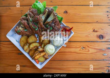German pork knuckle is served with baked potatoes and sauce inside a white ceramic plate placed on the dining room table to make the pork knuckle read Stock Photo