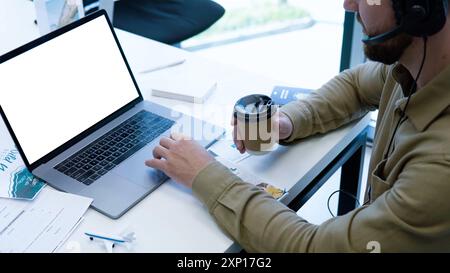 Cropped image of businessman working with blank white screen computer laptop while holding cup of coffee or tea. Mock up screen used for advertising. Stock Photo