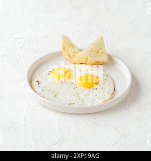 Two perfectly fried eggs with crispy bread on a white plate Stock Photo