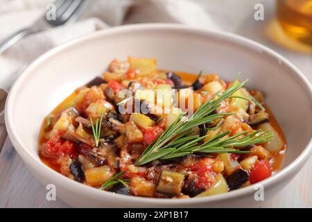 Bowl of ratatouille with aubergines, tomato, pepper, summer squash decorated with fresh rosemary in a table setting close-up Stock Photo