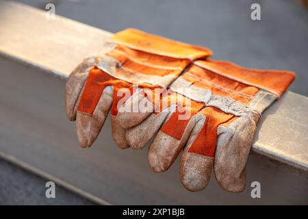 Yellow dirty work gloves on a metal bar stained with grease and oil. old dirty leather work gloves on metal bar background Stock Photo