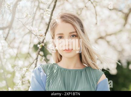 Portrait of young woman in the flowered garden in the spring time. Girl dressed in green dress Stock Photo