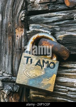 A rusty lock with the word Ti Amo written on it. The lock is attached to a wooden surface Stock Photo