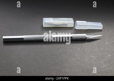Art knife that is used to work on paper and cardboard with extra set of blades on a plastic case isolated on a black background Stock Photo