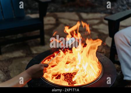 A closeup shot of a person roasting marshmallows over a fire pit during an outdoor gathering, with a blur background Stock Photo