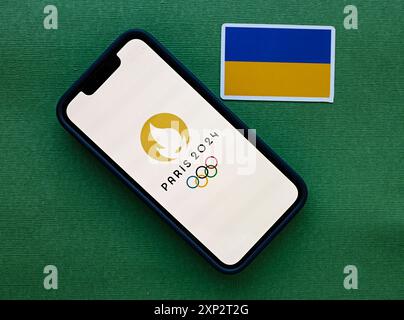 July 23, 2024, Paris, France. The logo of the 2024 Summer Olympic Games on the mobile phone screen and the flag of Ukraine. Stock Photo