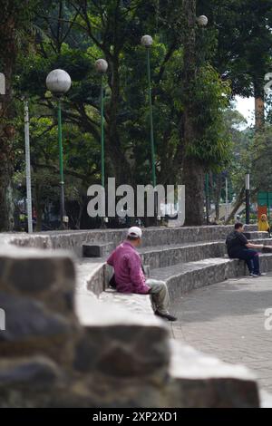 An old man sitting resting on a terraced bench in the middle of the city during the day Stock Photo