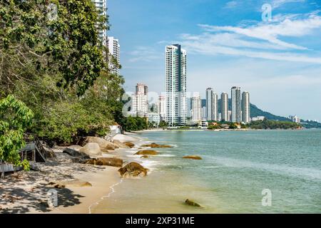 A view along Tanjing Tokong beach in Penang, Malaysia with tall, modern, skyscrapers, part of a city skyscape in the background. Stock Photo