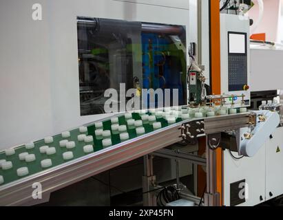 Plastic bottle caps on conveyor belt from plastic injection molding press machine. Industrial manufacturing. Stock Photo