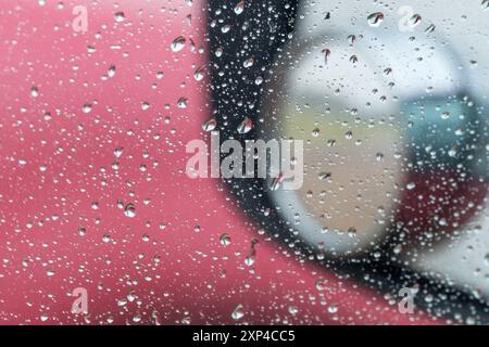 Raindrops on car window, side mirror reflecting a rainy day. Stock Photo