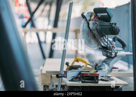 Professional circular saw on a wooden table. Carpenter's workspace in outdoor setting. Visible blade, opened machine and other tools Stock Photo