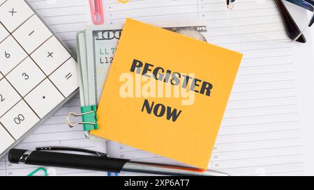 REGISTER NOW words written on a yellow sticker on American banknotes on the background of a business notebook Stock Photo