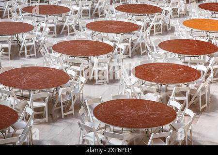 Rows of round dinner tables and chairs stand arranged in a bright hall waiting for guests. Stock Photo