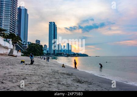 A view along Tanjing Tokong beach in Penang, Malaysia at sunset with the sun reflecting orange in the sea with a city skyscape in the background. Stock Photo