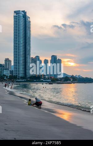 A view along Tanjing Tokong beach in Penang, Malaysia at sunset with the sun reflecting orange in the sea with a city skyscape in the background. Stock Photo