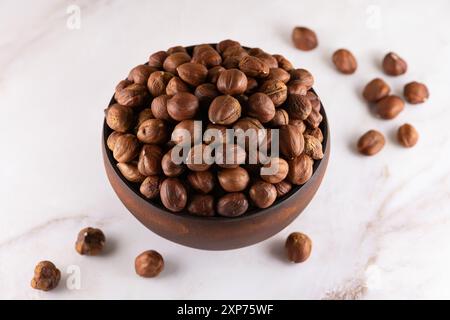 Hazelnuts in a wooden bowl on marble countertop. Whole, dried and shelled nuts of filbert, ready to eat as snack, close-up, high resolution. Stock Photo