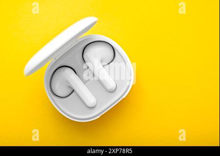 Top view of opened case with white wireless headphones on bright yellow background Stock Photo