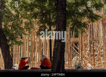 Construction workers sitting on break in front of bamboo scaffolding in Hanoi Vietnam Stock Photo