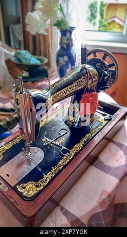 Moscow - July 20, 2024: Singer sewing machine in interior of an untidy room of country house. Close-up of hands. Stock Photo