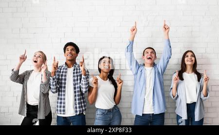 Teens pointing up on free space over white brick wall Stock Photo
