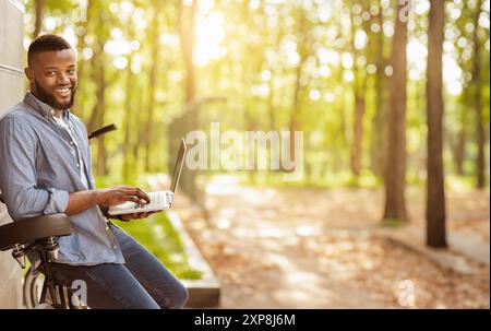 Handsome black man leaning on his bike and using laptop Stock Photo