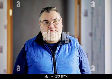 An angry plus size Caucasian man in her 40s wearing prescription glasses in home interior stands in hallway. Stock Photo