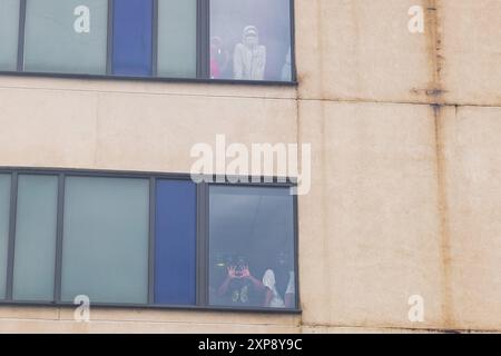 Rotherham, UK. 04 AUG, 2024. Persons housed in the hotel look out of the Windows towards the crowd  as hundreds of police and protestors clash outside a Holiday Inn Express on Manvers way, Rotherham. The right wing demonstrators, described by Sir Kier Starmer as 'thugs' set fire to property, smashed glass and fought with police for several hours. Multiple arrests and Injuries to rioters and police. Credit Milo Chandler/Alamy Live News Stock Photo