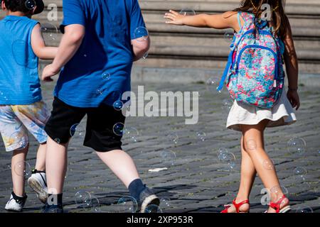 Girl and boy play with soap bubbles in a city square. Stock Photo