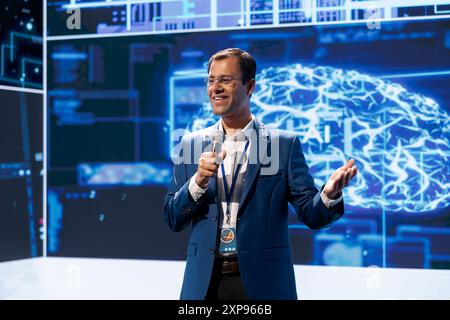 Cheerful engineer presenting how AI technologies can bring businesses increased productivity during conference. Jolly man using microphone to discuss about implementation of AI driven solutions Stock Photo
