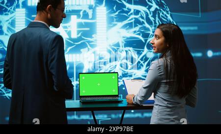 Startup coworkers brainstorming ways to use AI on chroma key notebook to improve data driven decisions. Technicians using mockup laptop to improve artificial intelligence tech, camera A Stock Photo