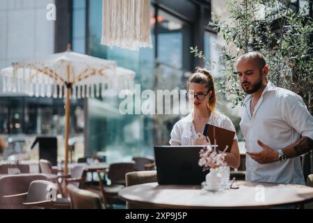 Business professionals working on laptop at outdoor cafe in urban city Stock Photo