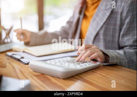 A close-up image of a businesswoman or a female accountant using a calculator and taking notes in her notebook, working at her desk in the office. Stock Photo