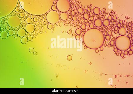 Macro photography of an oil and water mixture creating bubbles on a green, orange and yellow background. Stock Photo