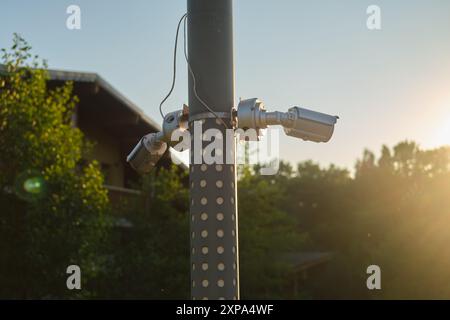Multiple surveillance cameras mounted on a pole outdoors with trees and a building in the background. Security equipment photography for design and pr Stock Photo