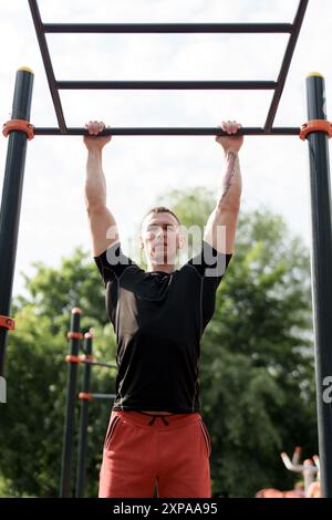 Determined man doing pull-ups at an outdoor fitness park Stock Photo