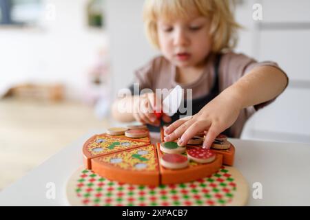 Boy playing with wooden toys in living room, serving and cutting pizza. Stock Photo