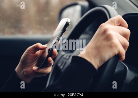 Closeup of female hands typing text message on cell phone while driving car through countryside landscape in winter, selective focus Stock Photo