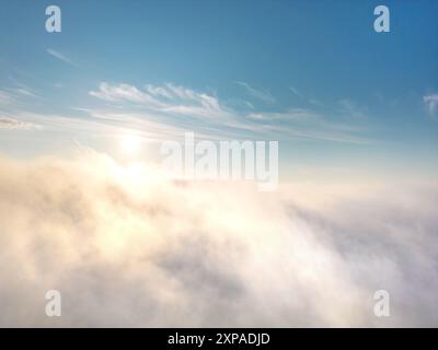 View from above of fog or clouds with clear blue sky and rising sun in the background Stock Photo