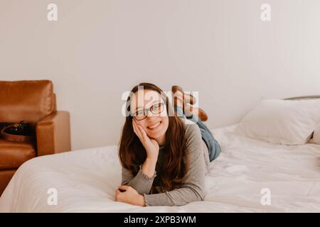 Smiling Hispanic young woman lying on bed, casual setting Stock Photo