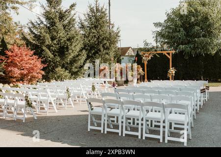 Outdoor wedding ceremony setup with white chairs and floral arch Stock Photo