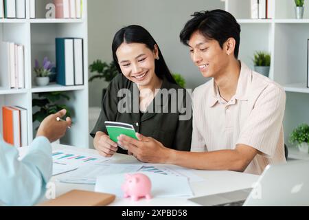 Young Couple Planning Savings with Financial Advisor, Reviewing Documents and Piggy Bank in Modern Office Stock Photo